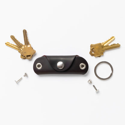 Brown leather key organizer with keys and accessories on a white background