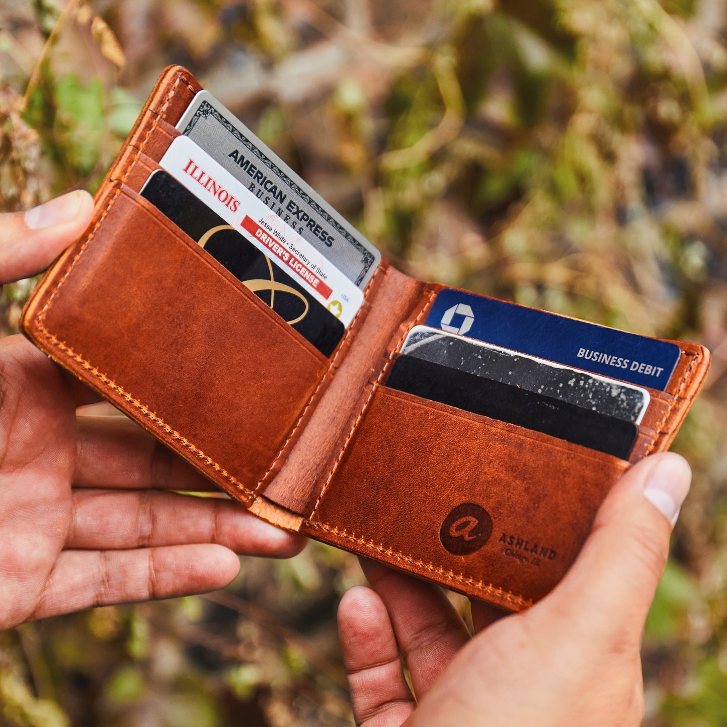 Brown leather wallet with cards held in hands against a blurred natural background