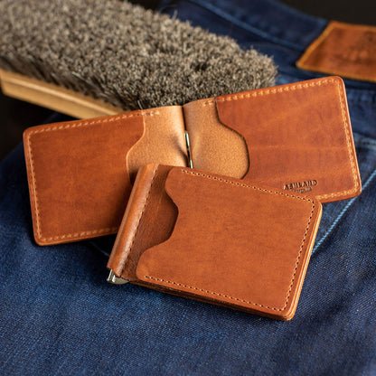 Several Capone Money Clips in English Tan Dublin sitting on blue jeans with a leather care brush