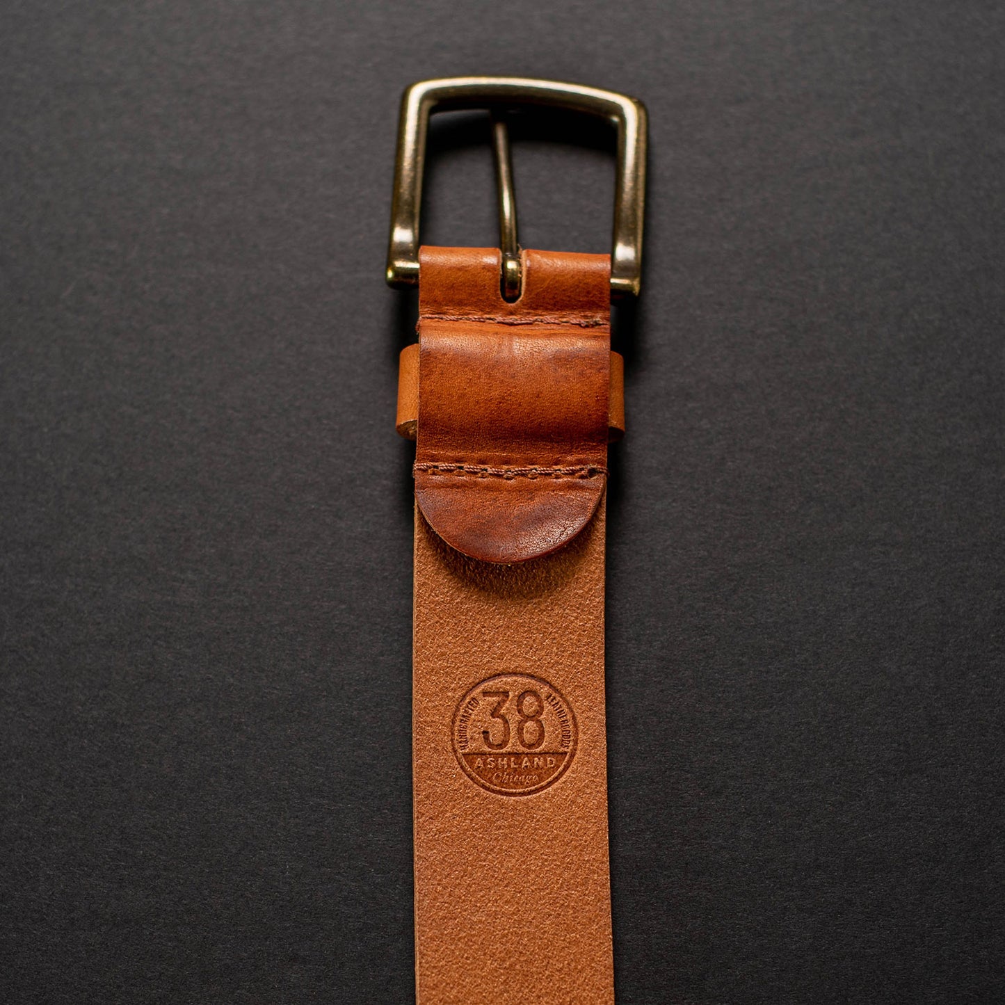 ashland leather belt laying vertically, showing back of buckle hardware with Size 38 stamp visible